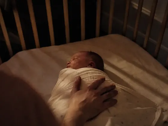 hand resting on a swaddled baby in a cot