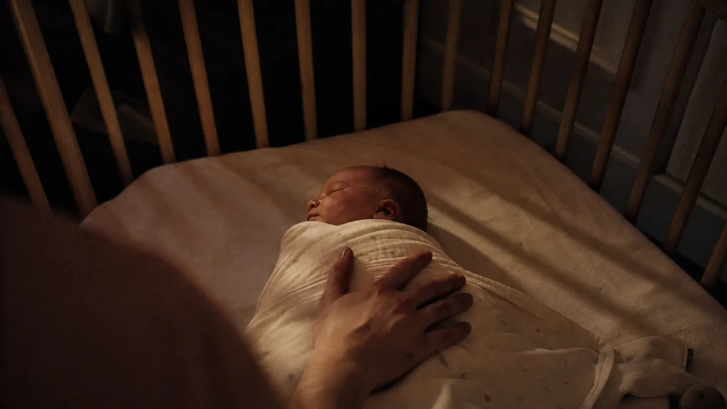 hand resting on a swaddled baby in a cot